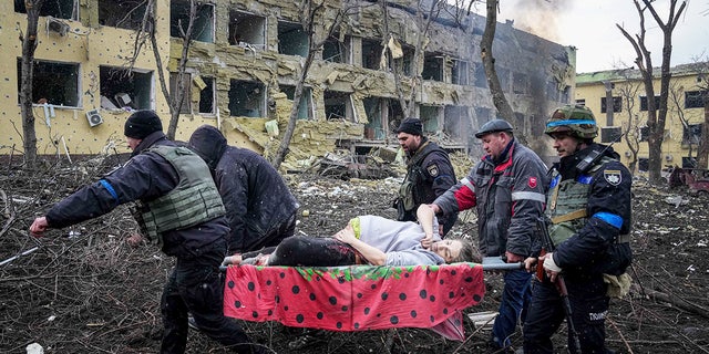 Ukrainische Einsatzkräfte und Freiwillige transportieren eine verletzte schwangere Frau, die vom Bombenanschlag auf das Entbindungsheim in Mariupol, Ukraine, betroffen war. 