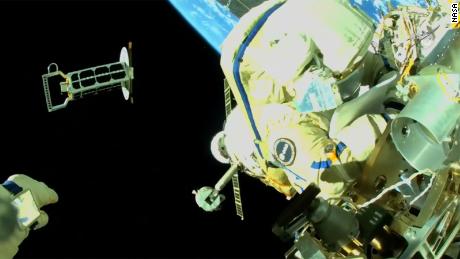 Cristoforetti ist zu sehen, wie er am Äußeren der Internationalen Raumstation arbeitet, während Artemyev, dessen Hand unten links zu sehen ist, einen Nanosatelliten in die Umlaufbahn wirft. 