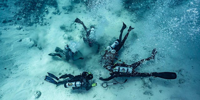 Taucher werden gezeigt, wie sie nach Schätzen graben, die auf dem Meeresgrund vergraben sind – der Ort eines Schiffswracks auf den Bahamas.