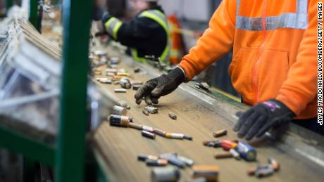 Mitarbeiter sortieren Batterien, die sich in einer Recyclinganlage über ein Förderband bewegen.